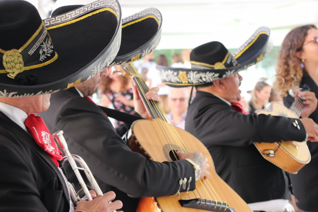 Primer plano lateral de músicos de mariachi tocando la trompeta, el guitarrón y la vihuela en un evento social.