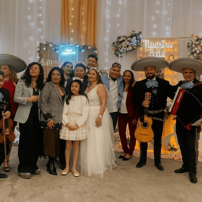 Texto Alt (Alt Text): Cuatro integrantes del Mariachi Reyes del Mediterráneo posando con trajes charros de color burdeos, moños negros con dorado y sombreros a juego. Sostienen violín, vihuela, guitarrón y trompeta en un pasillo elegante.