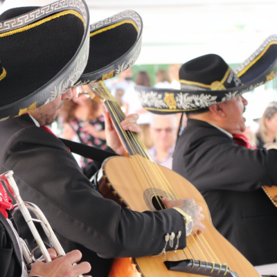 Primer plano lateral de músicos de mariachi tocando la trompeta, el guitarrón y la vihuela en un evento social.