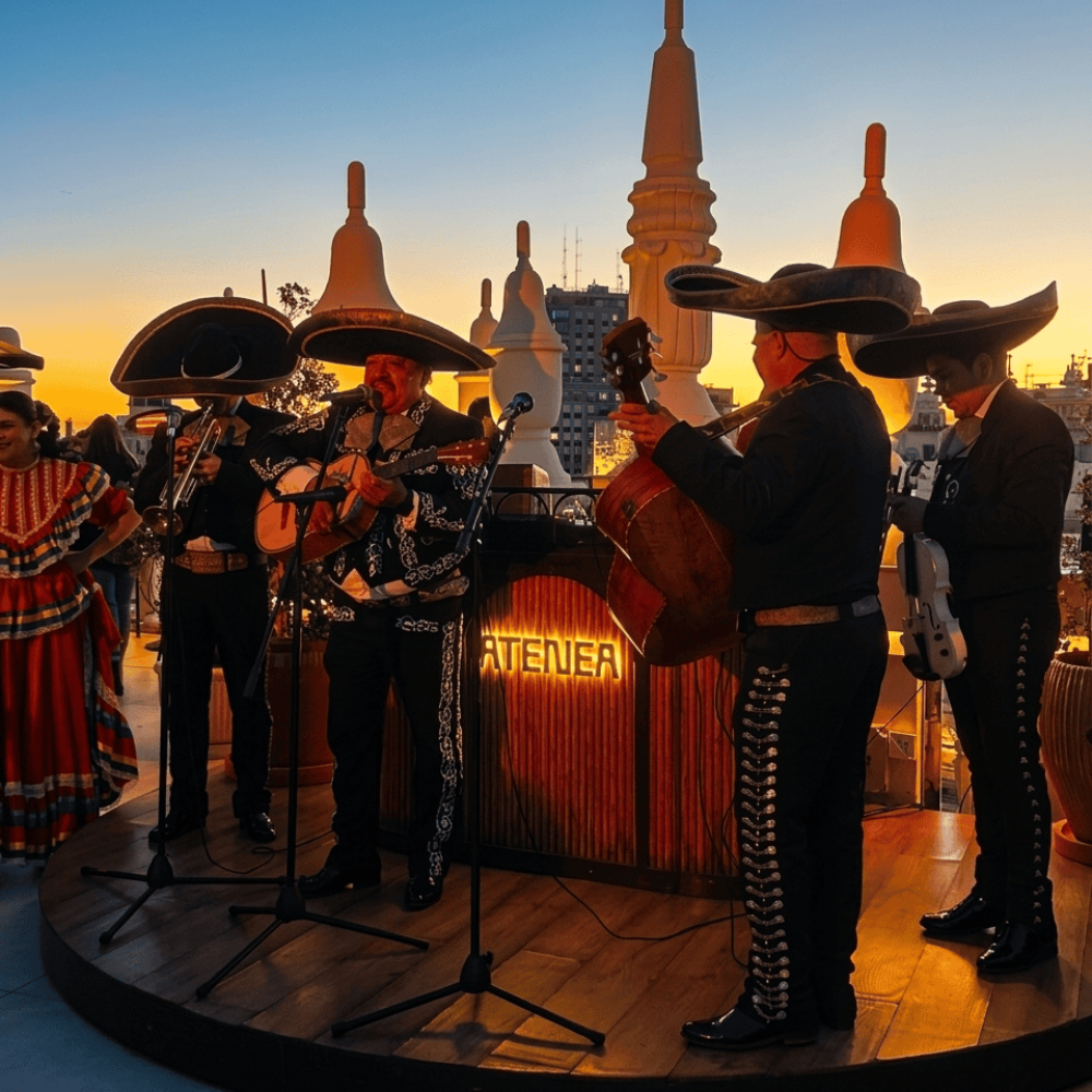 Mariachis en Elche | Serenatas, Bodas y Eventos 24H 52 Grupo de mariachis actuando en una terraza al aire libre durante el atardecer, con el cielo naranja de fondo y estructuras arquitectónicas blancas.