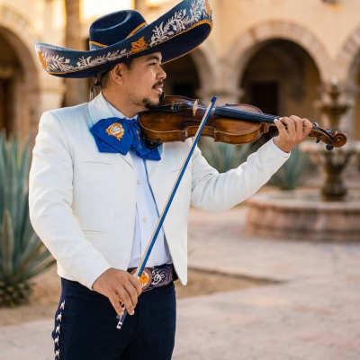 Músico mariachi tocando el violín con traje de charro blanco y sombrero bordado en un evento al aire libre.